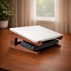Könnte beinhalten: Ein Laptop-Ständer aus dunklem Holz mit einem weißen Laptop und einer schwarzen Tastatur. Der Ständer hat ein minimalistisches Design. Der Laptop ist für ergonomisches Arbeiten angewinkelt. Die Tastatur befindet sich darunter.