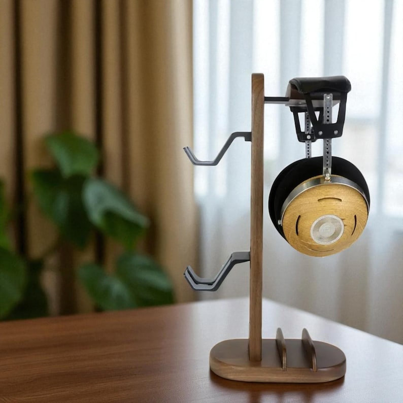 May include: A wooden headphone stand with a dark brown finish. The stand features two curved metal hooks for hanging headphones and a cradle for holding the headphones. A pair of headphones with a black ear cup and a wooden finish are displayed on the stand.