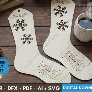 May include: Two wooden stocking-shaped cutouts with snowflake designs and the text "Candy Yarn". The cutouts have a laser-cut design at the bottom. A mug of coffee and pinecones are in the background. The image also includes the text "CDR + DFX + PDF + AI + SVG DIGITAL DOWNLOAD".
