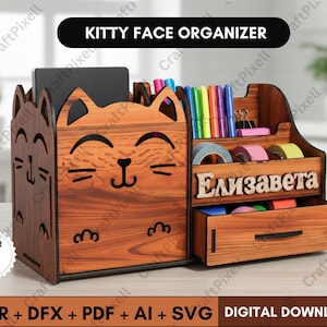 May include: Wooden kitty face organizer with multiple compartments, including a drawer and slots for pens and other supplies. The organizer has a cat face design and the text "Kitty Face Organizer".