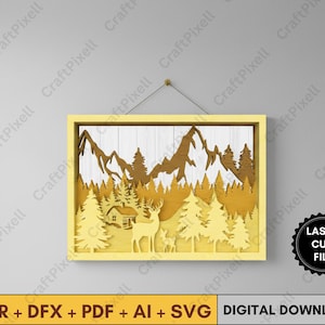 Könnte beinhalten: Ein geschichtetes Holzkunstwerk in einem gelben Rahmen zeigt eine Berglandschaft mit Bäumen, einer Hütte und Hirschen. Das Kunstwerk ist lasergeschnitten und enthält den Text "LASER CUT FILE" und "DIGITAL DOWNLOAD".
