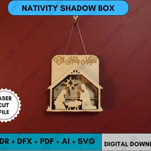 Puede incluir: Una caja de sombras de madera de la Natividad con el texto "Oh Holy Night". El diseño cortado con láser representa la Sagrada Familia y una estrella. La caja de sombras está suspendida por una cuerda sobre un fondo rojo. También se ven las palabras "Laser Cut File".