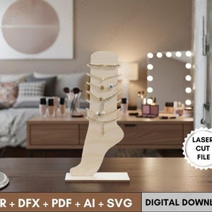Könnte beinhalten: Ein hölzerner Fuß-Schmuckständer mit mehreren goldfarbenen Fußkettchen. Der Ständer steht auf einem weißen Sockel und steht auf einer dunkelbraunen Oberfläche. Der Text "LASER CUT FILE" und "DIGITAL DOWNLOAD" sind sichtbar.