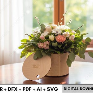 Puede incluir: Una caja redonda de madera con tapa, llena de un vibrante arreglo floral. Las flores incluyen margaritas blancas, claveles rosas y follaje verde. La tapa está parcialmente abierta. El texto "CDR + DFX + PDF + AI + SVG" y "DIGITAL DOWNLOAD" están en la parte inferior.