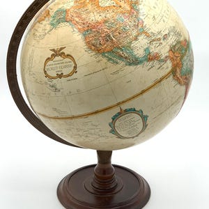 May include: A vintage 12-inch diameter globe with a cream-colored surface, featuring detailed geographical information. The globe is mounted on a dark brown wooden stand with a matching meridian ring. The text "World Classic Series" is visible.