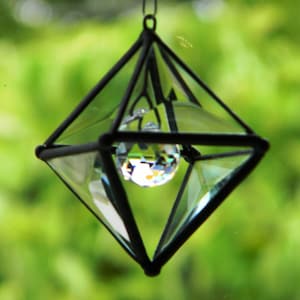 May include: A black metal and glass diamond-shaped prism with a clear crystal hanging inside. The prism is hanging from a string.