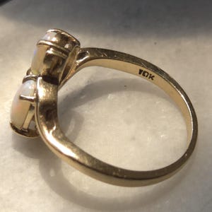 May include: A gold ring with two oval opals. The ring is marked "10K" and has a polished finish. The opals have a milky white and iridescent appearance.