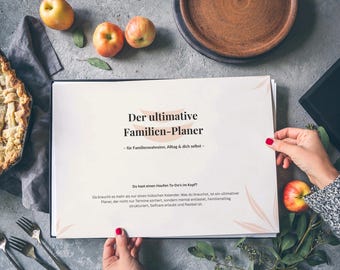 May include: A family planner with the text "Der ultimative Familien-Planer" is held by a person. The image includes a pie, apples, and a plate, suggesting a lifestyle or organizational theme. The planner is in German.
