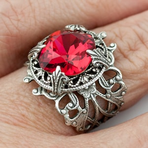 May include: A silver ring with a large, red gemstone set in a filigree design.
