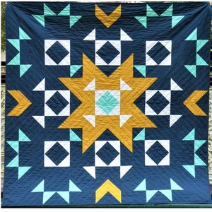 Può includere: Una trapunta con un motivo geometrico in tonalità di blu, bianco, giallo e verde. La trapunta presenta un grande disegno a stella al centro.