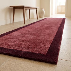 Alfombra de lana tejida a mano en tonos burdeos y rosa empolvado, con diseño de borde bicolor.