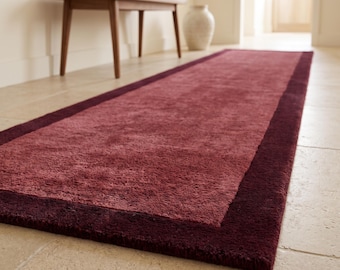 May include: A rectangular runner rug featuring a textured, dusty rose centre panel framed by a solid, dark burgundy border. The rug has a thick, plush pile and is laid out flat on a light-coloured stone floor, extending lengthwise into the room.