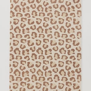 May include: Rectangular rug with a beige background and a repeating pattern of brown leopard spots. The spots vary in size and shape, creating a textured appearance. The rug is likely made of a soft material, suitable for a living room or bedroom.