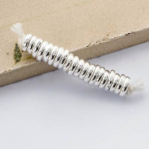 May include: A silver metal coil of beads strung on a white thread.