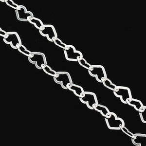 Puede incluir: Un collar de cadena de plata con eslabones en forma de corazón. La cadena es de doble capa y tiene un aspecto delicado y femenino.