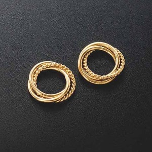 Puede incluir: Un par de pendientes de color dorado con un diseño de triple anillo. Los anillos están entrelazados y tienen un acabado liso y pulido.