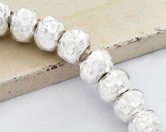 Può includere: Una collana di perline d'argento con una finitura testurizzata. Le perline sono infilate su un cordoncino bianco.