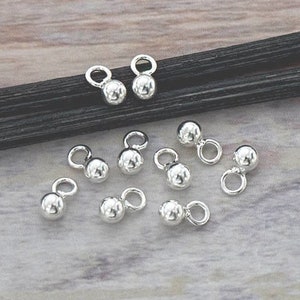 May include: Ten silver ball bead caps with a loop on top. The bead caps are arranged on a black surface.
