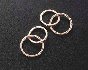 May include: Four rose gold textured rings interlocked on a black surface. The rings are circular and have a hammered texture. The rings are likely jewelry components or decorative elements.