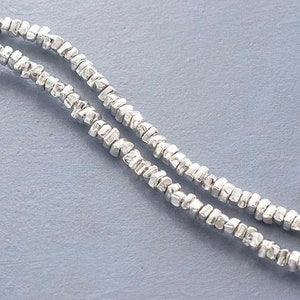May include: A silver chain necklace made of small, textured beads. The chain is double-stranded and has a delicate, minimalist look.