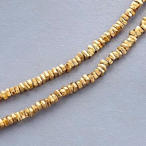 Peut inclure: Un collier en chaîne dorée composé de petites perles carrées texturées.