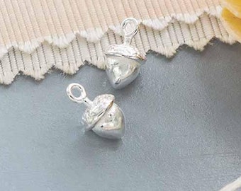 May include: Two silver acorn charms with a textured surface. The charms are on a light gray background.