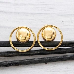 May include: A pair of gold earrings with a circle design and a small sphere in the center.