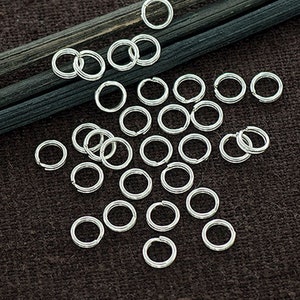 Op de afbeelding: Een close-up van een groep zilveren springringen op een donkerbruine stoffen achtergrond. De springringen zijn in de vorm van een ster gerangschikt.