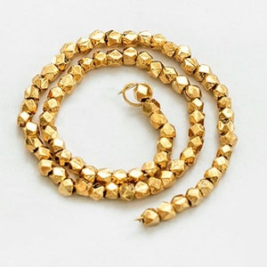 May include: A gold necklace made of small, faceted beads. The necklace is coiled into a circle and has a small clasp.
