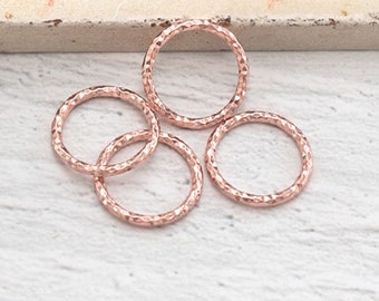 May include: Five rose gold jump rings with a textured finish. The rings are arranged in a loose pile on a white surface.