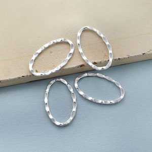 May include: Four silver oval-shaped rings with a textured, wavy design. The rings are on a light brown surface.