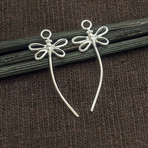 May include: Two silver dragonfly shaped earring findings with a loop at the top and a long, thin wire extending from the bottom.