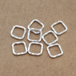 May include: A group of eight silver-toned metal jump rings with a hammered texture. The rings are square shaped and have a smooth, polished finish.