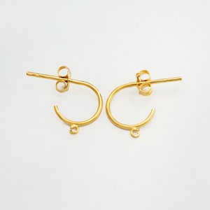 May include: A pair of gold-toned hoop earrings with a jump ring at the bottom of each hoop. The earrings have a post back closure.