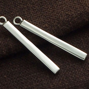 May include: Two silver bar earrings with a simple, minimalist design. The earrings are made of a smooth, polished metal and have a slightly rounded edge.