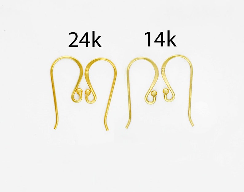 Op de afbeelding: Twee paar goudkleurige metalen oorhaken, waarbij het linkerpaar is gelabeld met 24k en het rechterpaar met 14k. Elke haak heeft een gebogen draadontwerp met een klein bolletje aan de basis voor het bevestigen van sieradenonderdelen.