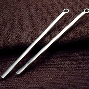 May include: Two silver, straight, long, thin, bar-shaped pendant charms with a small loop at the top.