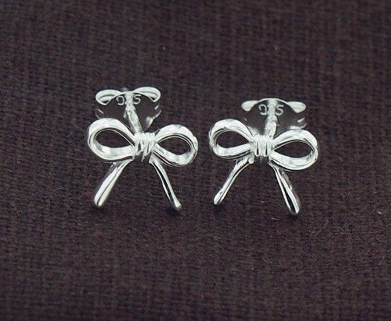 May include: A pair of silver bow-shaped stud earrings. The earrings are marked with "925" on the back.