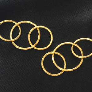 以下が含まれることがあります： 黒い背景に、金色のハンマーテクスチャの円形イヤリングが2組あります。 各セットは、3つの相互接続された円で構成されています。 イヤリングは明るく光沢のある仕上がりで、光を反射します。