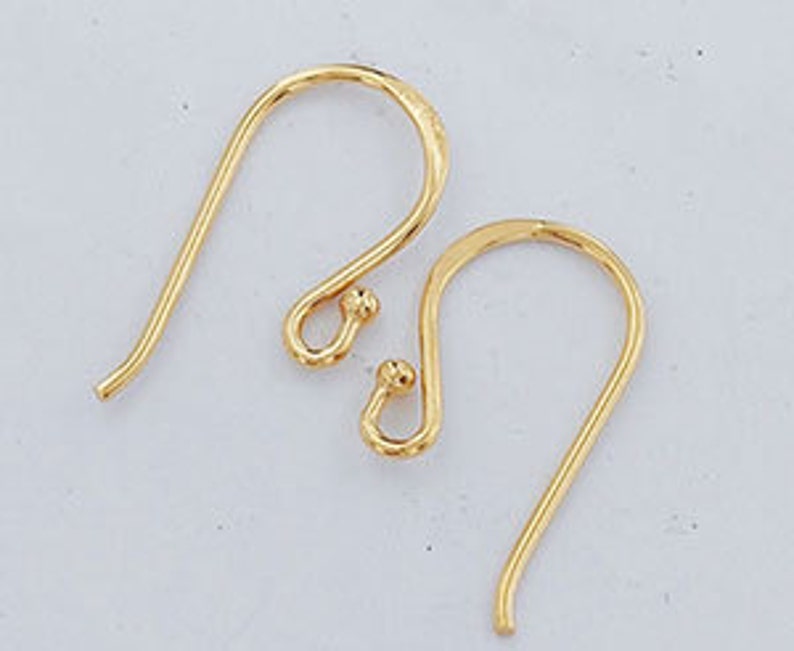 Op de afbeelding: Twee goudkleurige oorhaken, elk met een gebogen draadontwerp met een klein bolvormig accent aan de basis van de lus. Deze sieradenonderdelen zijn ontworpen voor het bevestigen van decoratieve elementen om afgewerkte oorbellen te maken.