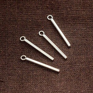 May include: Five silver metal jump rings with a straight bar attached to each ring. The jump rings are approximately 1.25 cm in diameter.