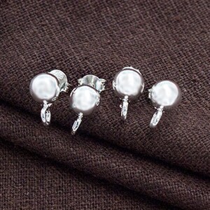 May include: Four silver earring backs with a round ball shape. The earring backs are on a brown fabric surface.