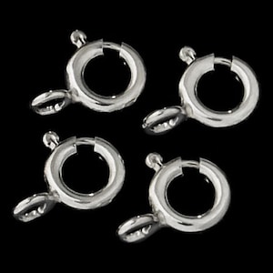 May include: Five silver-toned jump rings, also known as lobster clasps, are shown against a black background. The rings are circular with a small opening on one side and a spring-loaded clasp on the other.