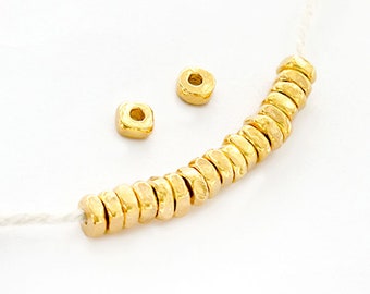 May include: A strand of gold-colored beads with a hammered texture. The beads are strung on a white cord and there are two extra beads off to the side.