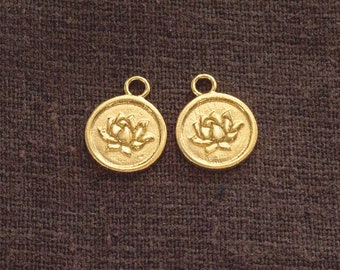 May include: Two gold-colored metal charms with a lotus flower design. The charms are round and have a loop at the top for attaching to a necklace or bracelet.