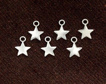 May include: Seven silver star-shaped charms with a loop at the top. The charms are all the same size and shape, and they are arranged in a semi-circle on a brown surface.