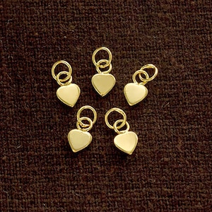 May include: Six gold heart-shaped charms with jump rings. The charms are approximately 1 cm in size.