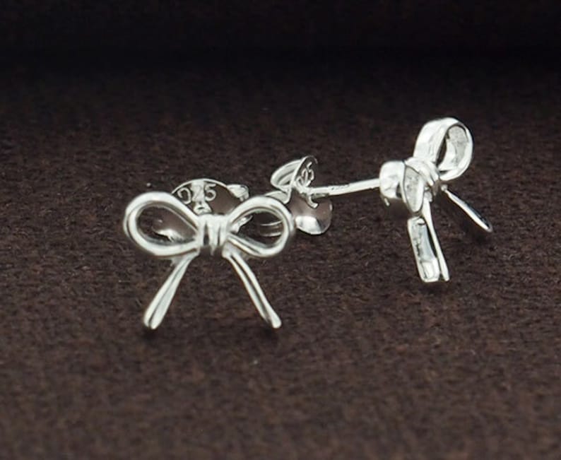 May include: A pair of silver bow-shaped stud earrings. The earrings are made of sterling silver and have a simple, elegant design.