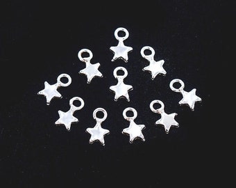 May include: A group of ten silver star-shaped charms with a loop at the top. The charms are arranged in a loose circle on a black background.