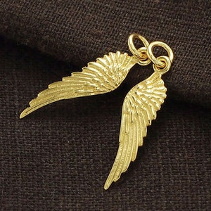 May include: A pair of gold angel wings charm pendant. The wings are detailed with a textured surface and have a loop at the top for attaching to a necklace or bracelet.